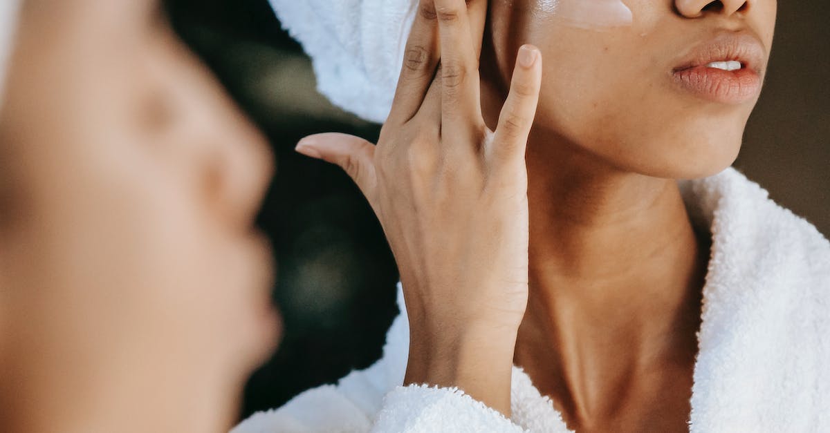 Does Irelia's Q apply W effects? - Crop unrecognizable young ethnic female in terry robe applying moisturizing cream on cheek while reflecting in mirror