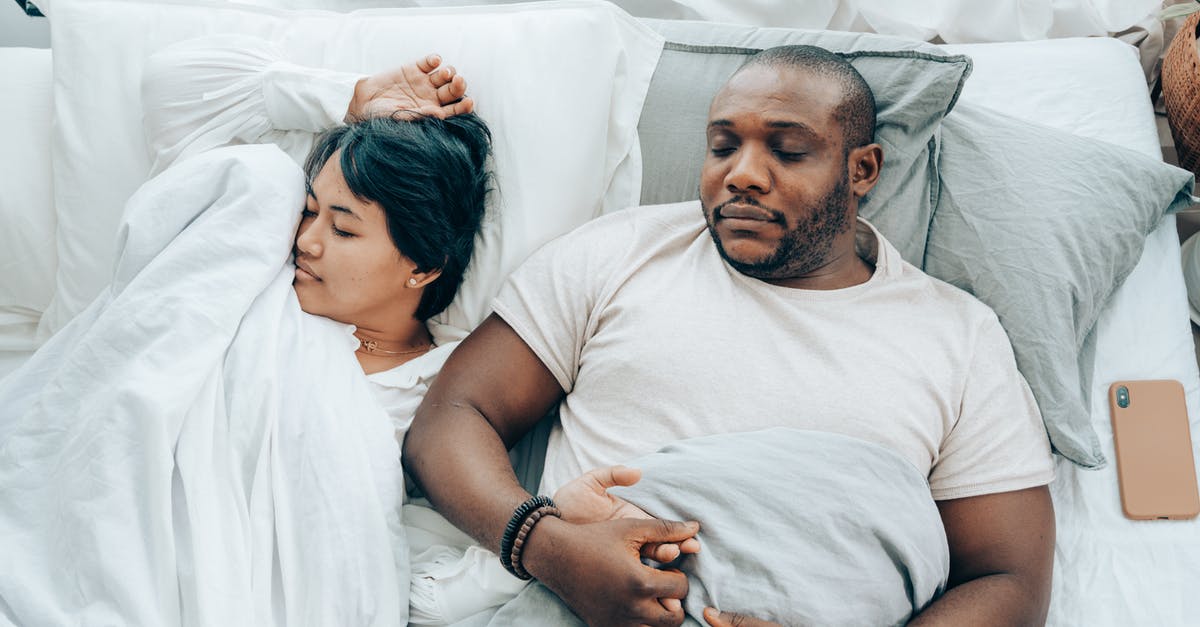 Does lying in a bed and not sleeping the whole night reset one's spawn? - Young multiethnic spouses sleeping in bed holding hands