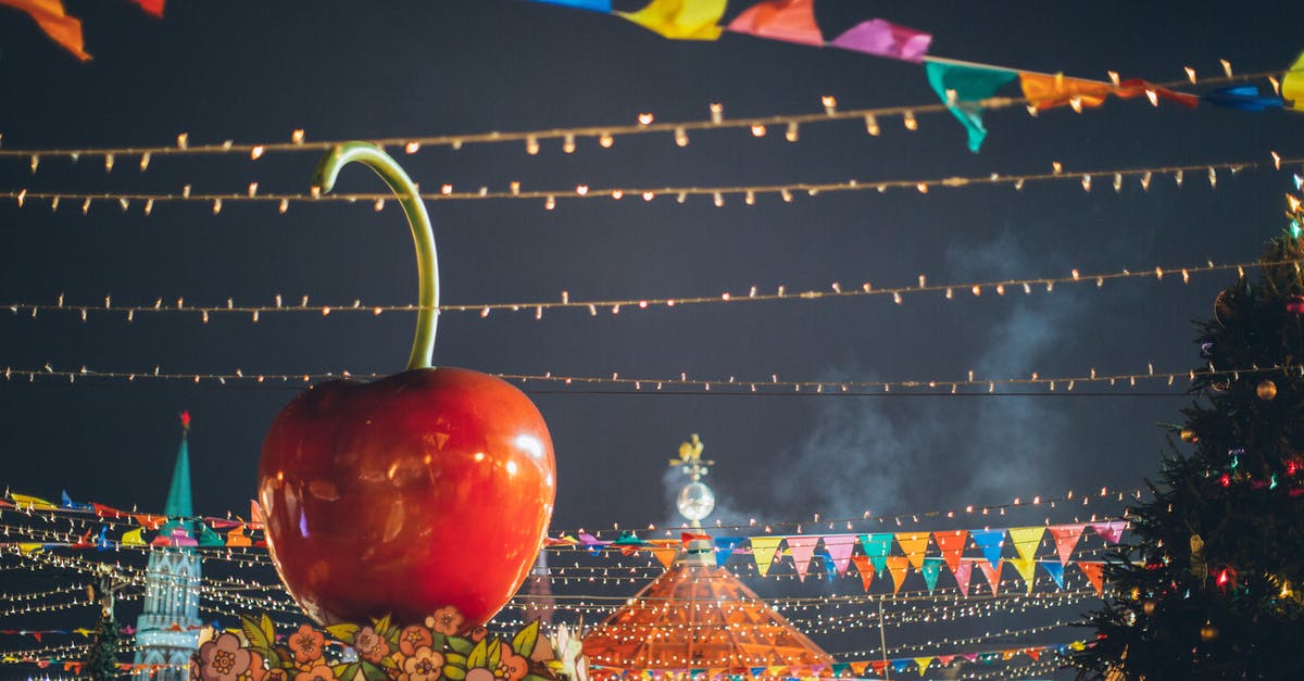 Does my miniature giant space piglet do anything? - Big red glossy toy apple on roof of building on fairground against dark sky in evening city park decorated to winter holidays