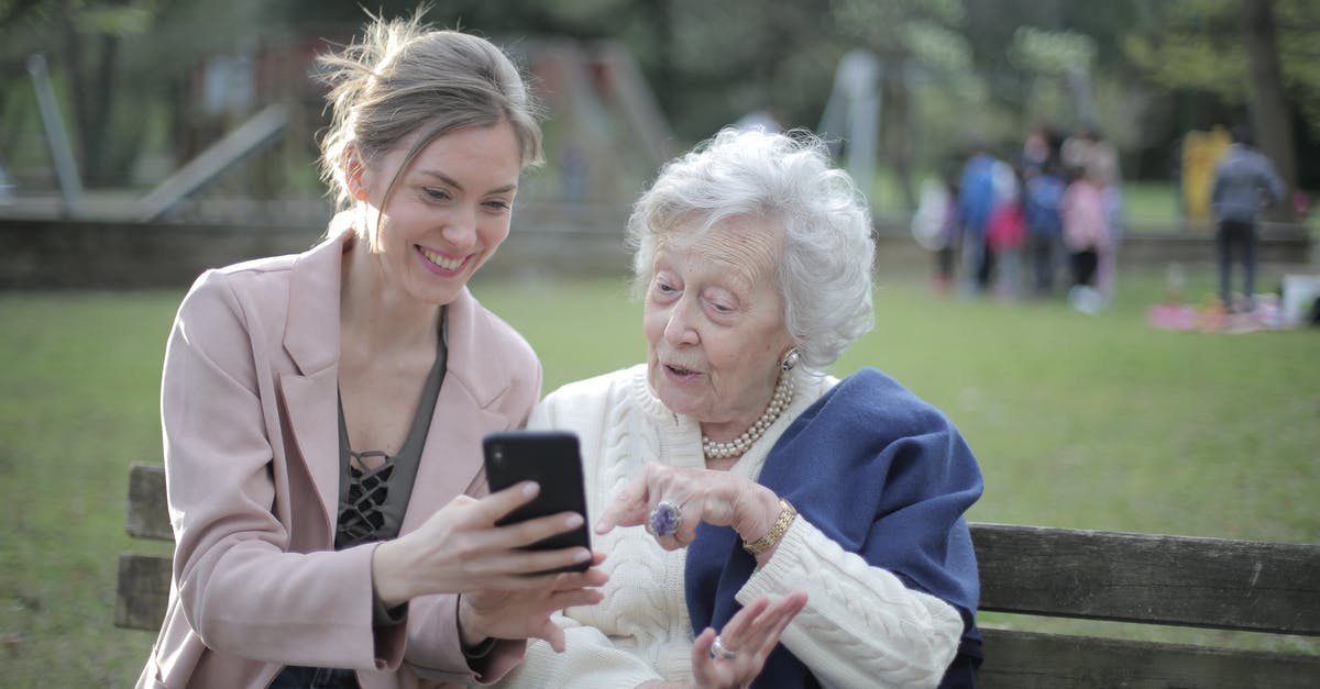 Does PES/FIFA support online multiplayer for older versions? - Delighted female relatives sitting together on wooden bench in park and browsing mobile phone while learning using