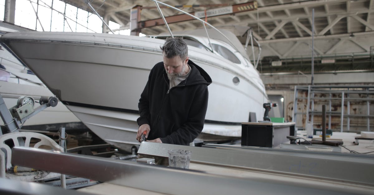 Does repairing the ship before scrapping yield better results? - Concentrated bearded adult workman in casual wear working with metal detail near boat in garage