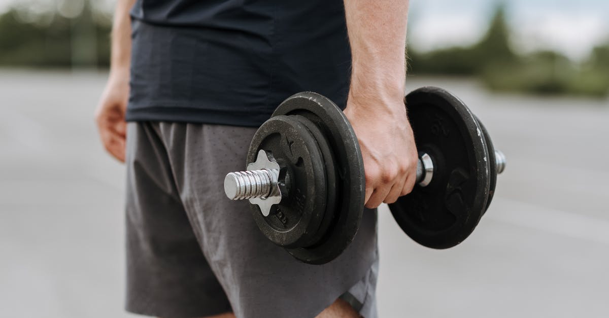 Does the current progress towards the next skill level carry over when training? - Crop anonymous male in activewear lifting heavy iron dumbbell on blurred background of street
