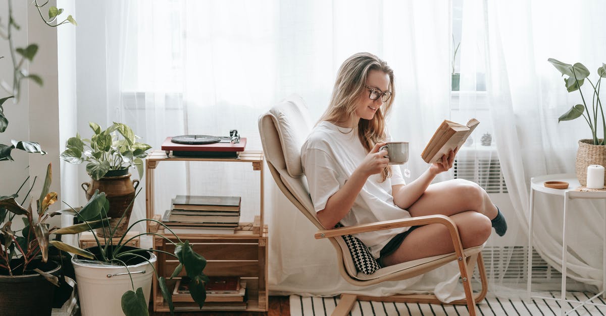 Dragon Age Inquisition Content installing - Cheerful young female in eyeglasses with cup of beverage reading textbook in armchair between potted plants in house room Dragon Age Inquisition Content installing - Cheerful young female in eyeglasses with cup of beverage reading textbook in armchair between potted plants in house room