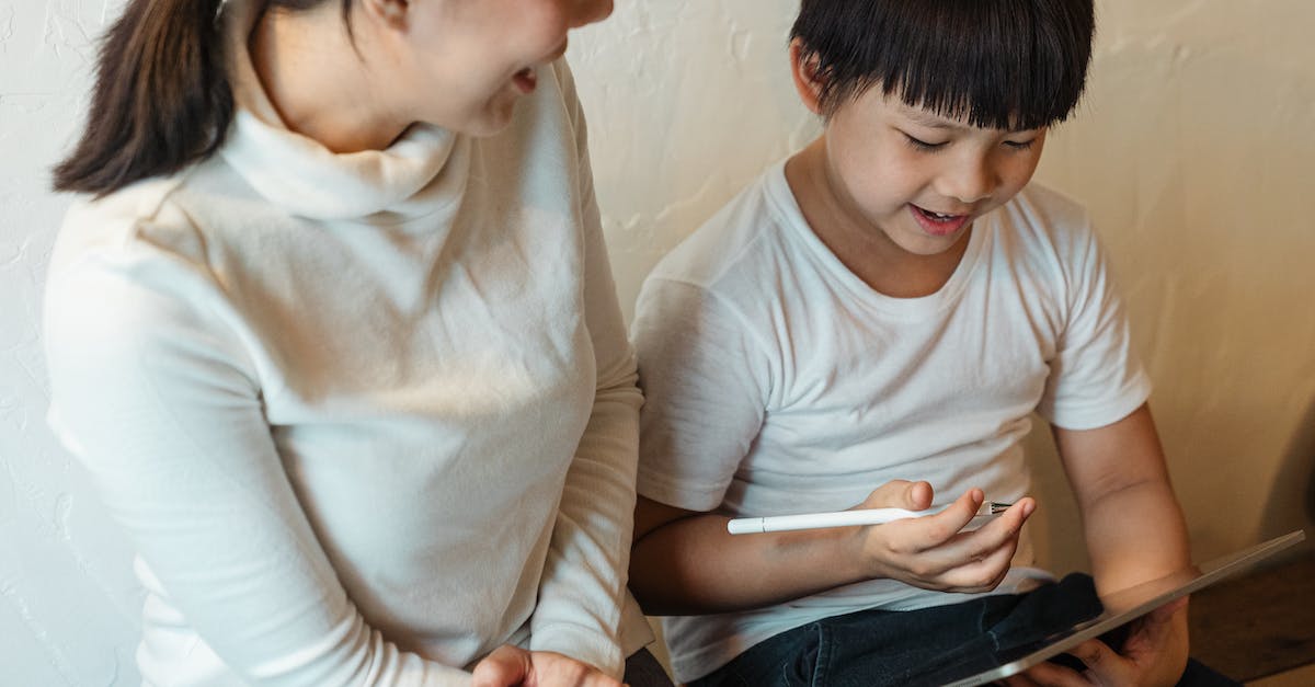 Dragon help in Skyrim. Can't escape - From above of crop glad mother in casual clothes sitting near cheerful ethnic boy with pen and tablet while using social media in house