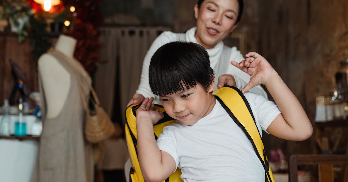 Dragon help in Skyrim. Can't escape - Cheerful ethnic woman helping content schoolboy in casual wear putting on yellow rucksack while standing at home decorated with garland and looking away