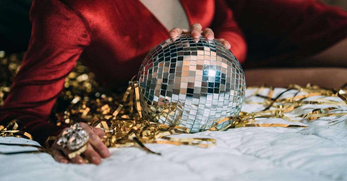 Dropping the disco ball to achieve accidental kill - Crop anonymous male in red velvet dress of drag queen lying on bed with glass disco ball