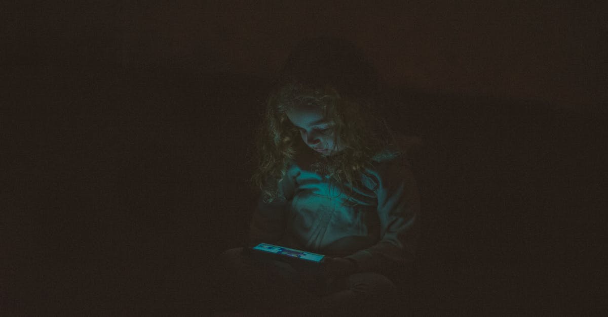 Duration of defensive pacts in late game - Focused  little girl with long curly hair in casual clothes sitting and using smartphone while watching video in dark room