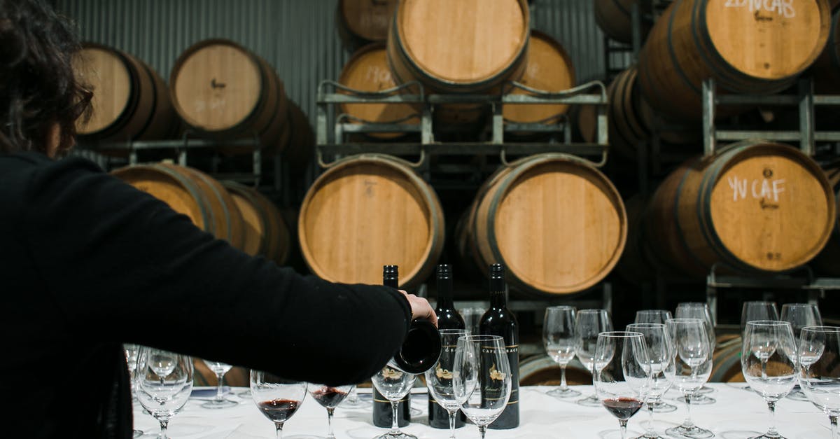 Dwarves not drinking booze in barrels right next to them - Back view of anonymous sommelier pouring wine from bottle into wineglass while standing at table with glassware in winery against barrels