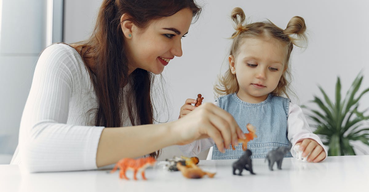 Early and Late game Runes - Adorable little girl sitting at white table with mother while playing with small toy wild animals for early education and development during spending time together at home