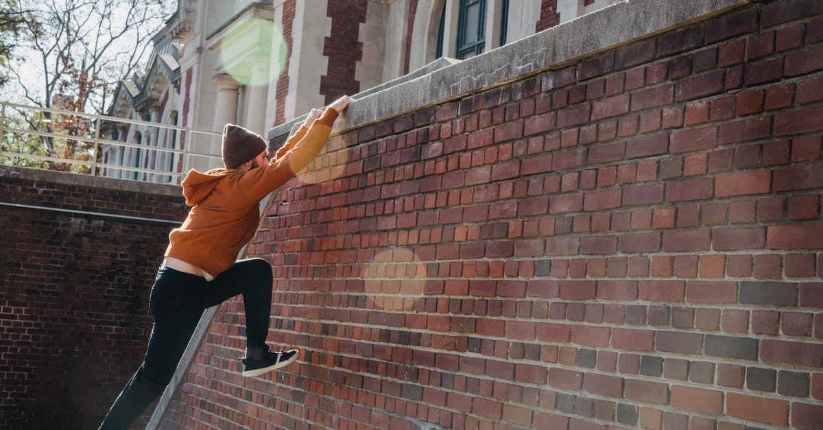 Effectively training multiple formations - Side view full body of determined male in hat jumping on wall and grabbing onto railing during training on street