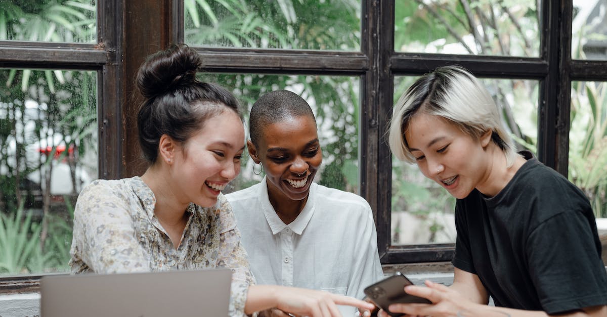 Effects of using black separation crystal? - Cheerful young diverse female friends laughing while watching funny video on smartphone during coffee break in cozy cafe