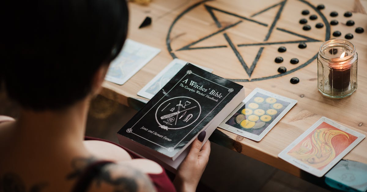 Enchanted Book separation - From above back view of crop unrecognizable female soothsayer with magic book at table with tarot cards at home Enchanted Book separation - From above back view of crop unrecognizable female soothsayer with magic book at table with tarot cards at home