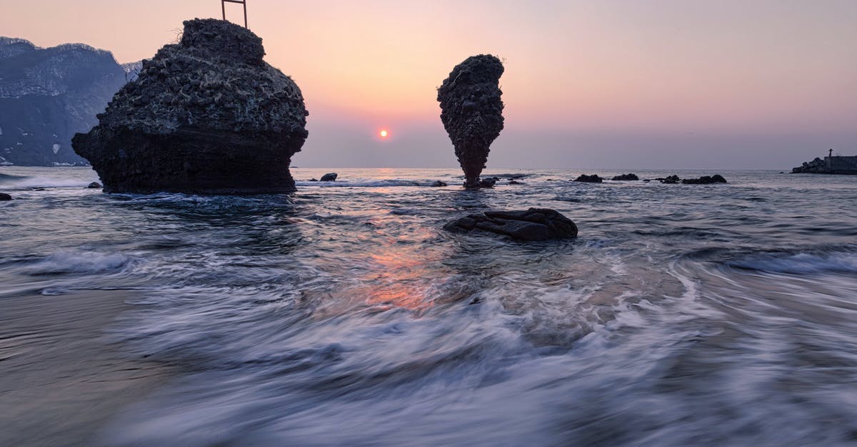 endless legend no watchtowers - Long exposure of small vibrant Sun in light blue pink sky over mountain range and cliffs next to coast of endless wavy ocean in evening at dawn endless legend no watchtowers - Long exposure of small vibrant Sun in light blue pink sky over mountain range and cliffs next to coast of endless wavy ocean in evening at dawn