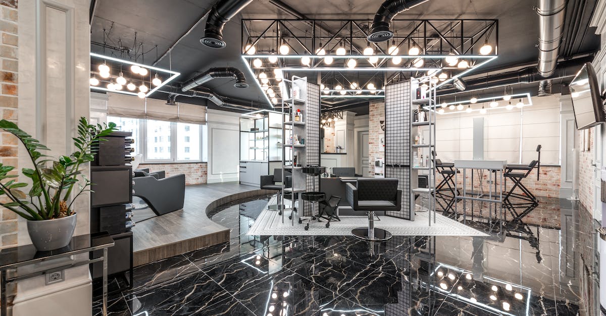 Essential kits not working - Black leather chairs placed in spacious stylish barbershop with bright glowing lamps and creative design with cosmetology products on shelves