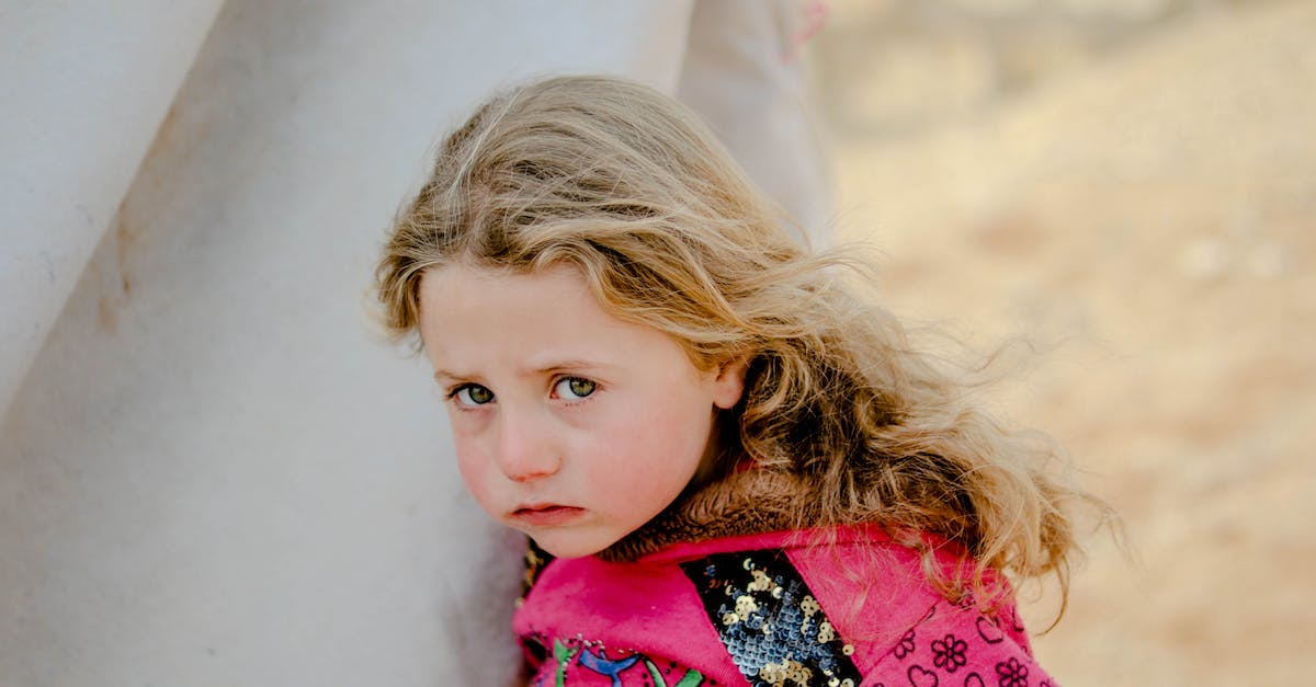 Fallout Shelter drafty in here, problem? - Unhappy little girl looking at camera while standing near weathered shelter in poor refugee camp on blurred background of countryside Fallout Shelter drafty in here, problem? - Unhappy little girl looking at camera while standing near weathered shelter in poor refugee camp on blurred background of countryside