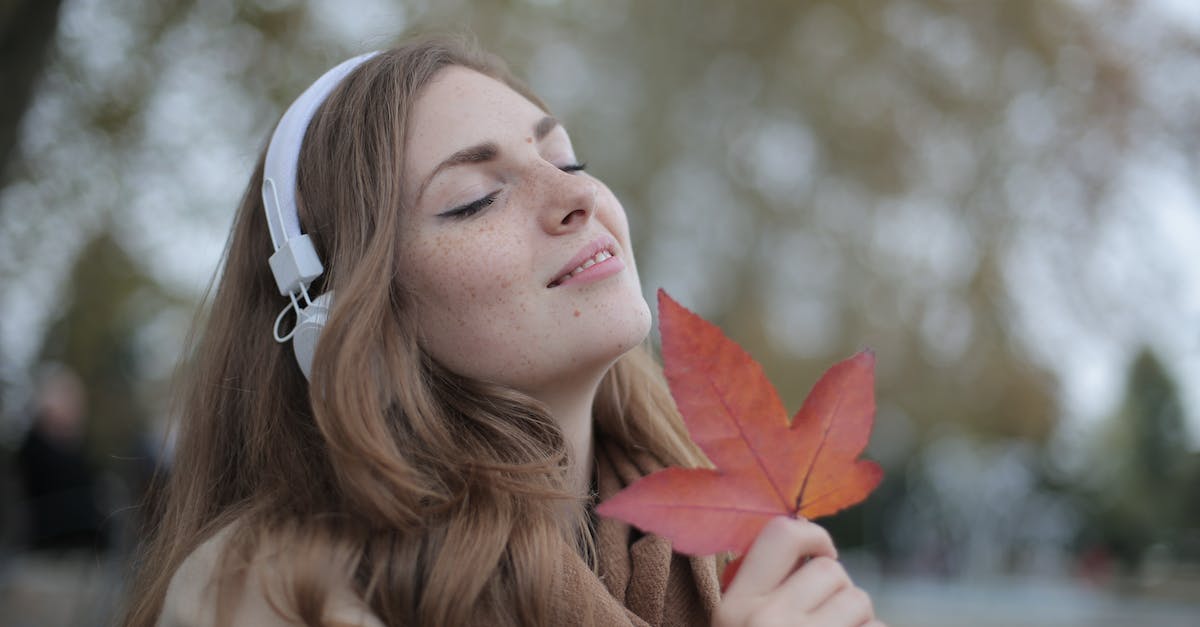 Fastest way to acquire Cracked red eye orbs? - Young satisfied woman in headphones with fresh red leaf listening to music with pleasure while lounging in autumn park