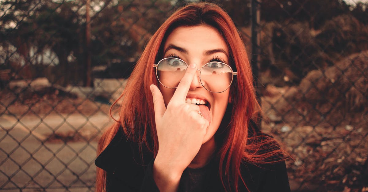 Fix strange behavior on roundabouts? - Young playful female in eyewear with red hair making face and sticking tongue out while fixing glasses looking at camera on street