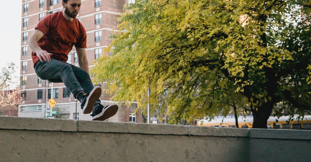 For the Vault Cards' Manufacturer-related challenges, grenades don't count? - Agile male athlete in casual outfit jumping above fence during training against urban building