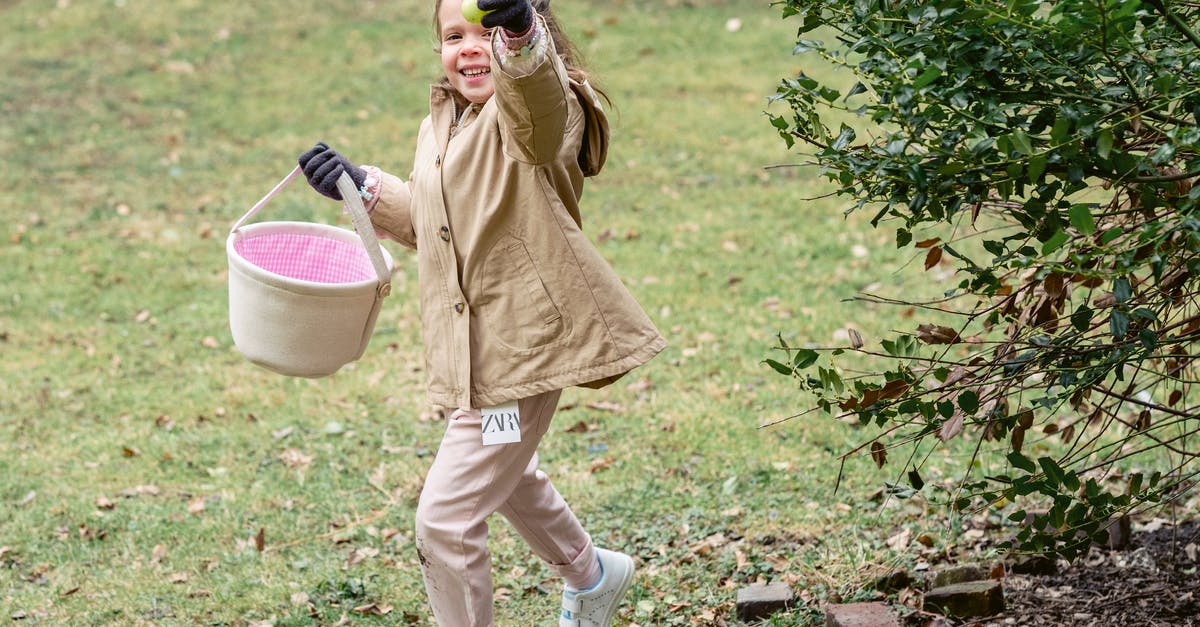 Found UAV, what is the purpose? - Full length cheerful girl in warm clothes carrying fabric basket and demonstrating ripe green colored egg or Easter egg in spring park