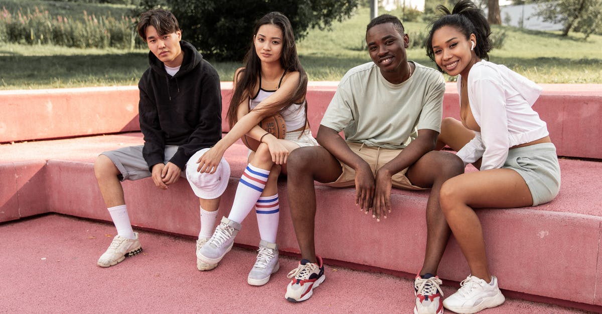 Free for all mode, allow team killing - Full body cheerful young multiracial friends in casual clothes sitting together on pink stone bench in green sunny park and looking at camera contentedly Free for all mode, allow team killing - Full body cheerful young multiracial friends in casual clothes sitting together on pink stone bench in green sunny park and looking at camera contentedly