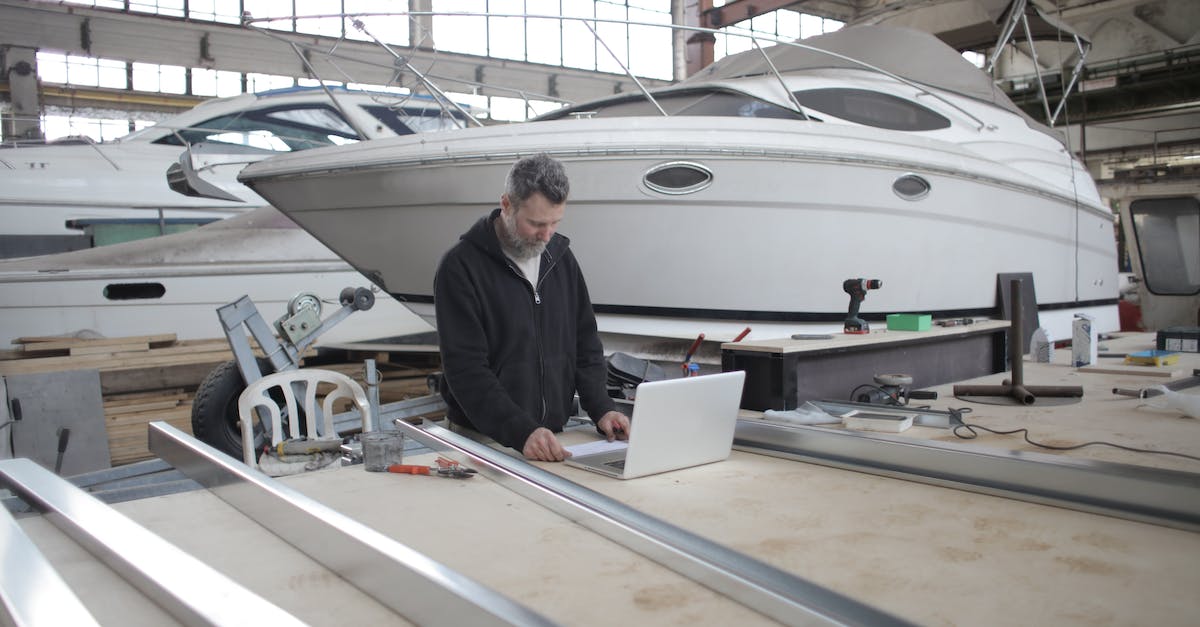 FreeOrion ship production variables - Adult worker using laptop at workbench during work in boat garage