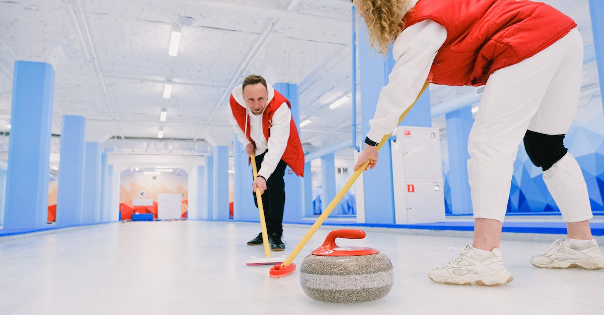 Frozen, Immobilized, anything else that stops you from moving? - Low angle of male and female players sweeping ice sheet with brooms in path of granite stone during curling training
