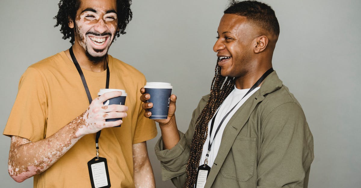 Gender labels on trainer badges in Pokémon Go - Cheerful black man with vitiligo skin laughing and drinking coffee with androgynous black man with afro braids against gray background