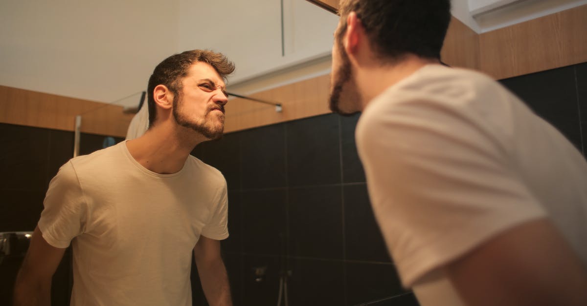 Geometry dash question about daily level - Low angle side view of young bearded male in casual shirt standing in bathroom and looking at with frown mirror in morning