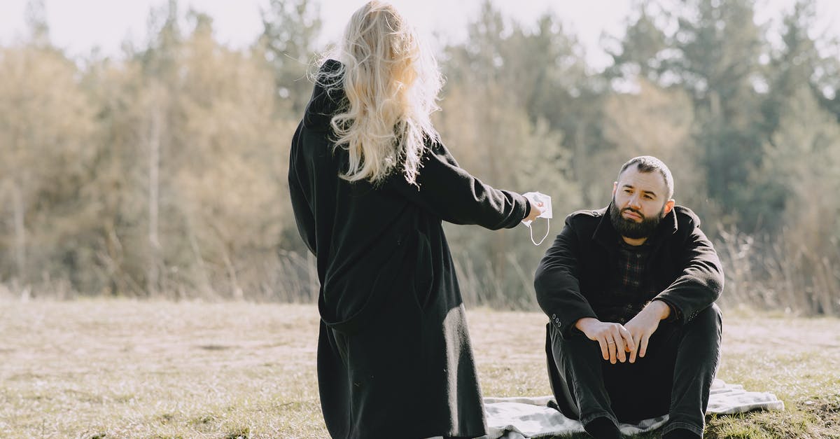 Give Undead mobs instant health - Blond girlfriend in back lit wearing black warm coat passing medical protective mask to boyfriend while spending time together in rural lawn during coronavirus outbreak