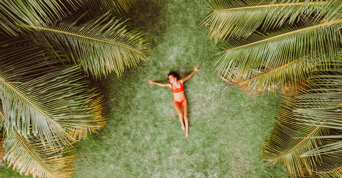 Grass doesn't grow - Woman lying on green grass among palms at resort Grass doesn't grow - Woman lying on green grass among palms at resort