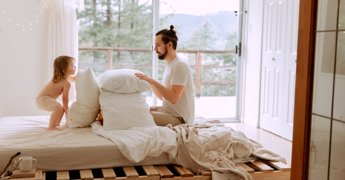Harrim's quest - siding with kobolds - Side view of serious bearded father in casual clothes playing with little child with pillows on comfortable bed in light bedroom at home