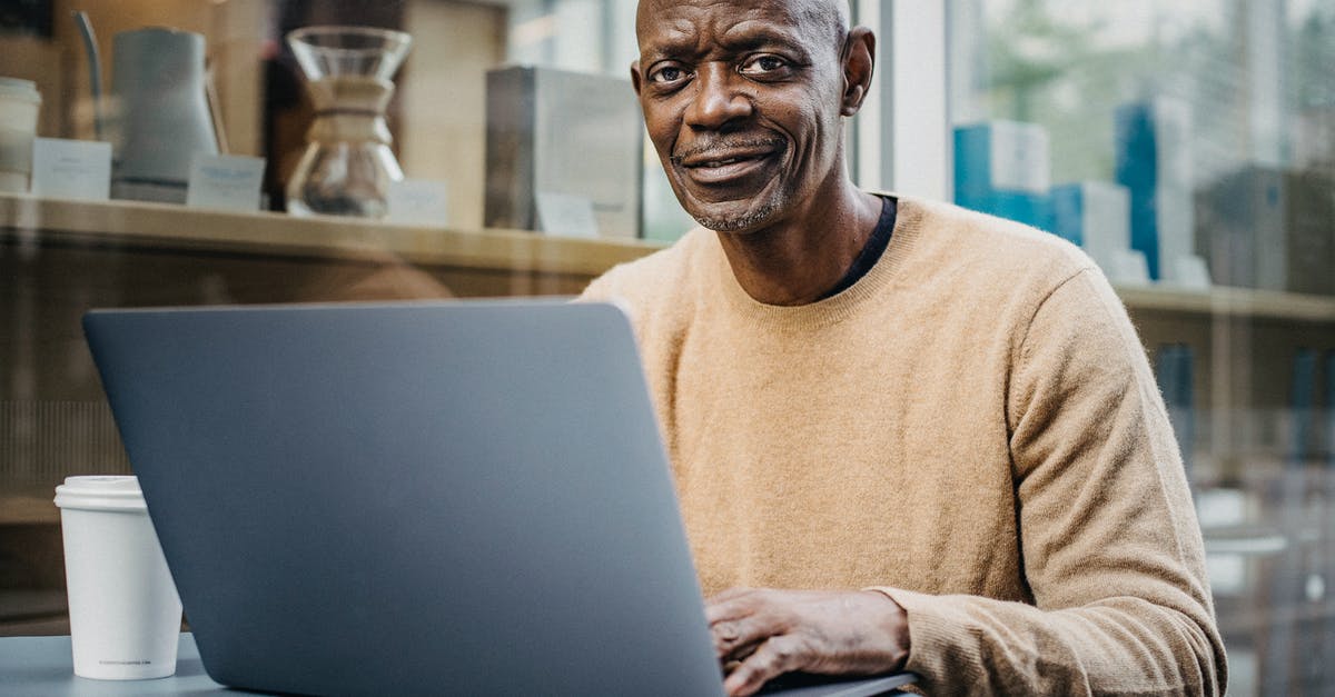 Has Pokémon GO changed their distance algorithm? - Positive mature bald African American male freelancer smiling and looking at camera while working on laptop sitting in cafe with cup of takeaway coffee