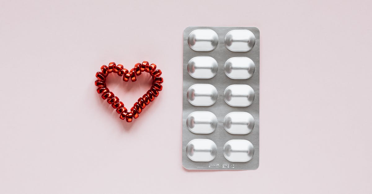 Heart containers which are painful to miss? - Top view of plastic blister with medical pills placed near red heart made of spiral elastic for hair on pink background