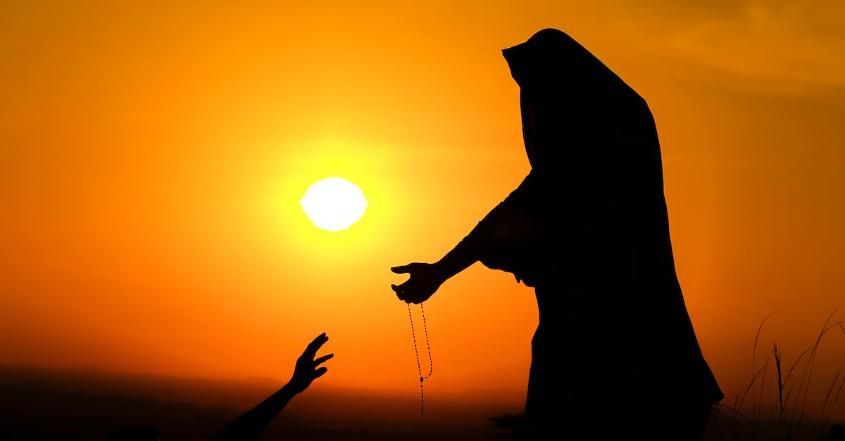 Help! I got lost in Nether! - Silhouette of unrecognizable female in traditional outfit stretching arm with beads to person against bright sunset sky Help! I got lost in Nether! - Silhouette of unrecognizable female in traditional outfit stretching arm with beads to person against bright sunset sky