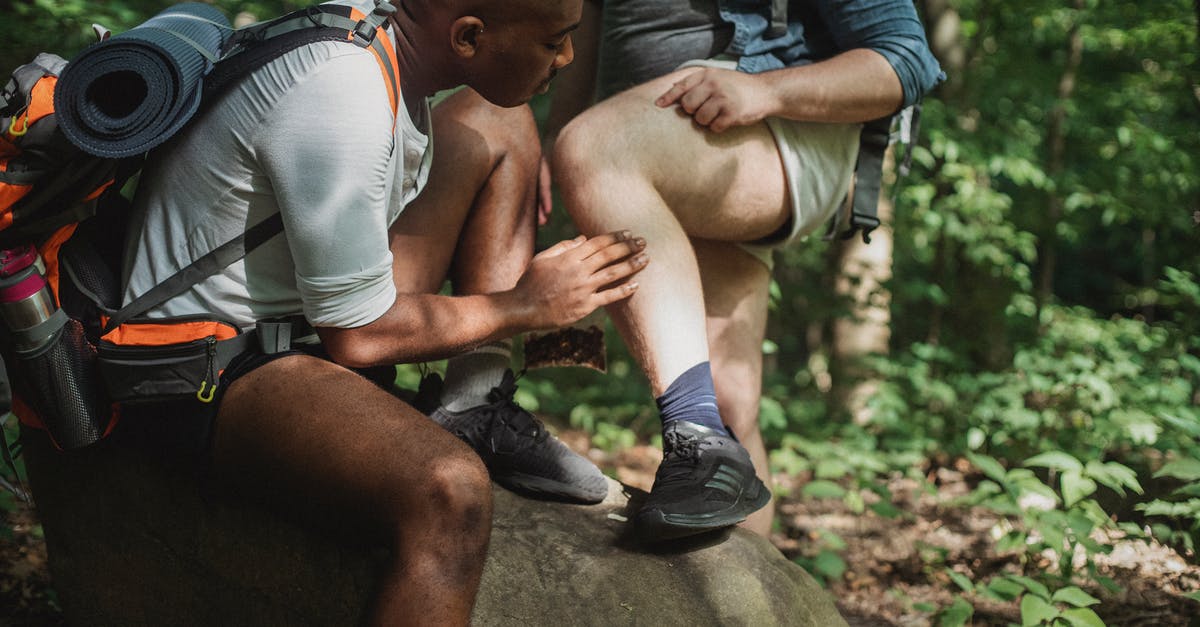 Help on the Earth Stone quest! - Multiracial men in activewear with backpacks resting on stone and checking ticks while having break during trekking