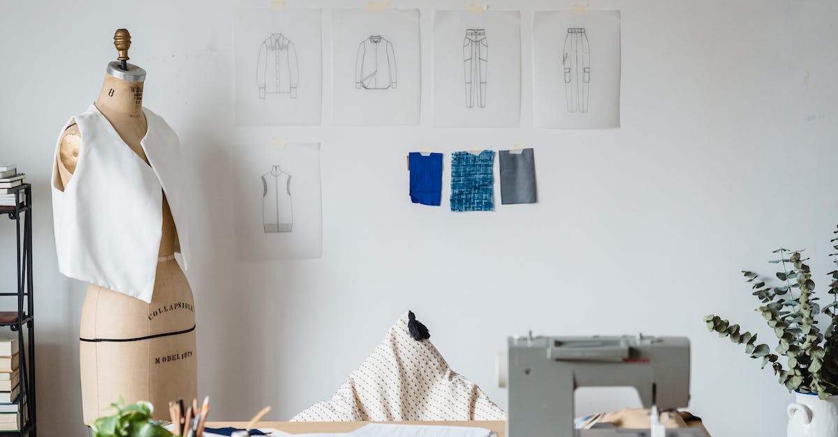 Help with textile industry - Table with sewing machine placed near mannequin with garment at white wall with drafts of cloth and samples of textile Help with textile industry - Table with sewing machine placed near mannequin with garment at white wall with drafts of cloth and samples of textile