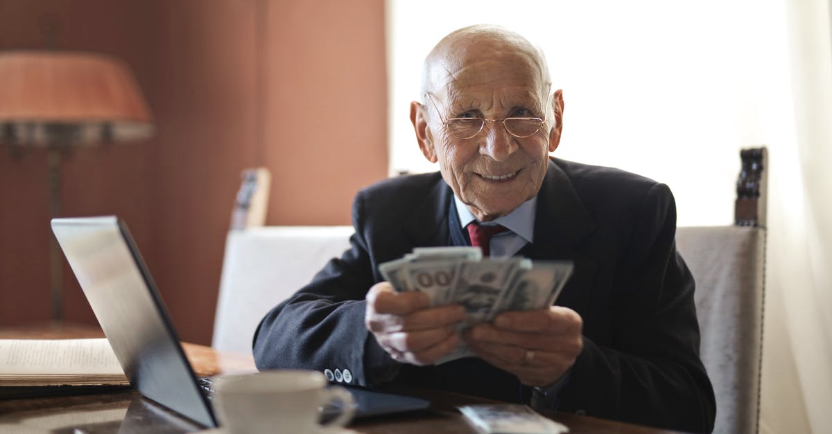 Highest paying career - Confident senior businessman holding money in hands while sitting at table near laptop Highest paying career - Confident senior businessman holding money in hands while sitting at table near laptop