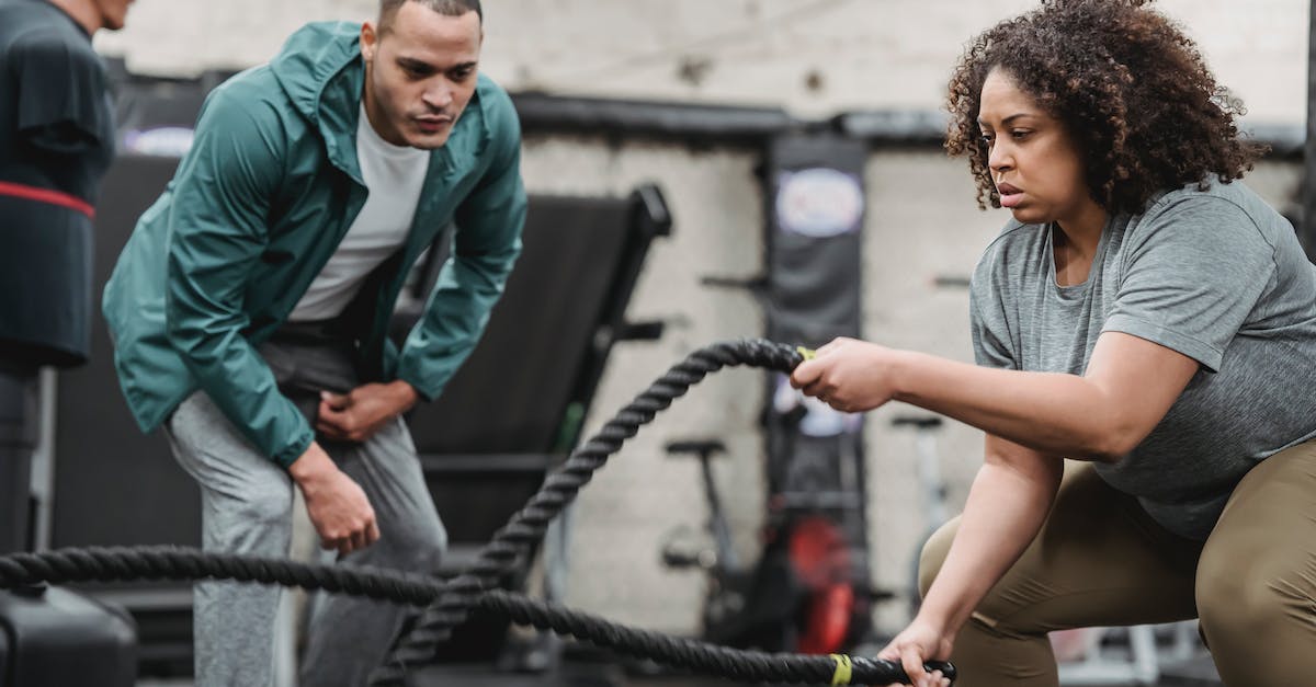 How are Clash of Clans multiplayer battles determined - Plus sized African American female in sportswear exercising with battle ropes near serious male instructor during intense workout in modern fitness center