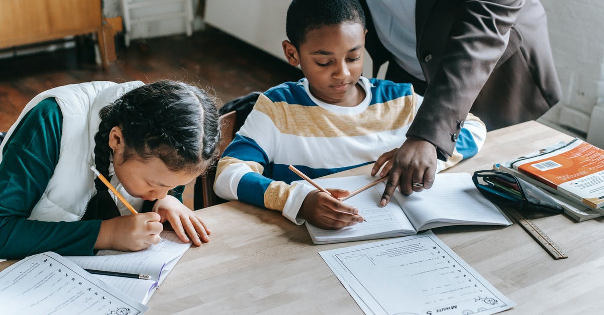 How are decimal point gains handled? - High angle of crop unrecognizable black female teacher explaining task to focused little schoolboy sitting at desk near attentive Asian classmate writing in notebook