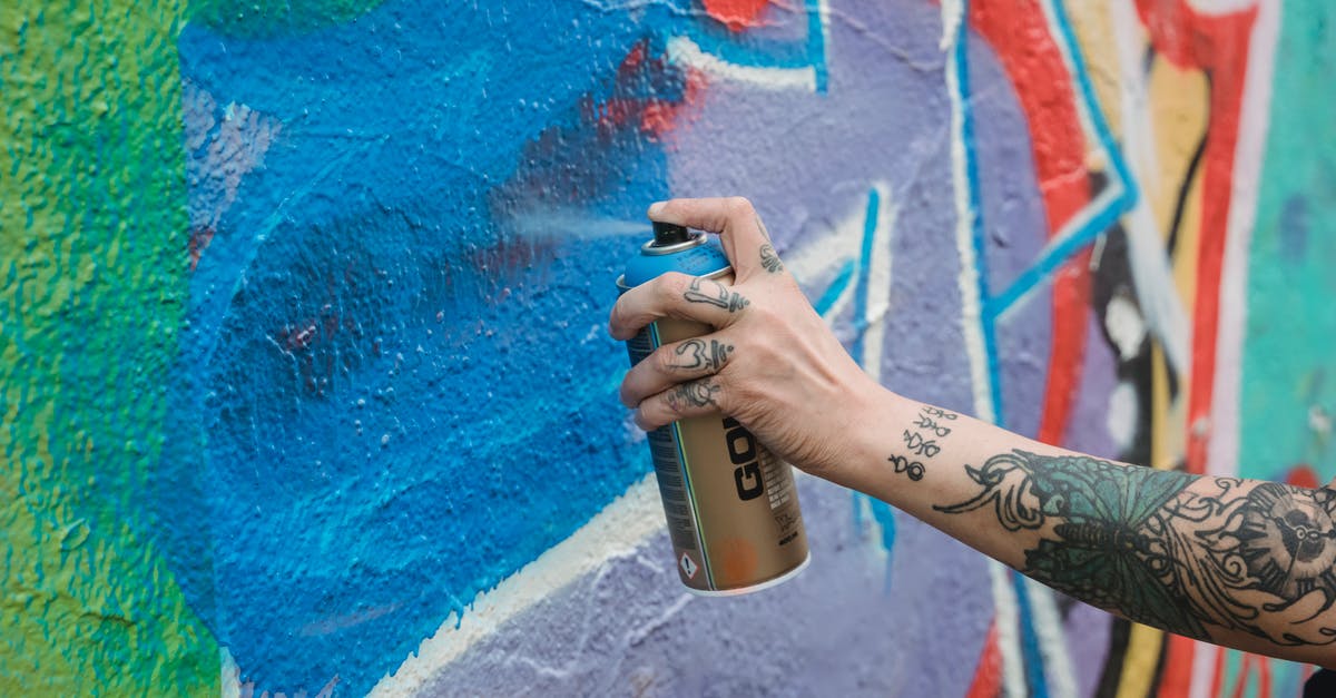 How can I access co-op skill games? - Crop unrecognizable tattooed painter spraying blue paint from can on multicolored wall with creative graffiti while standing on street in city