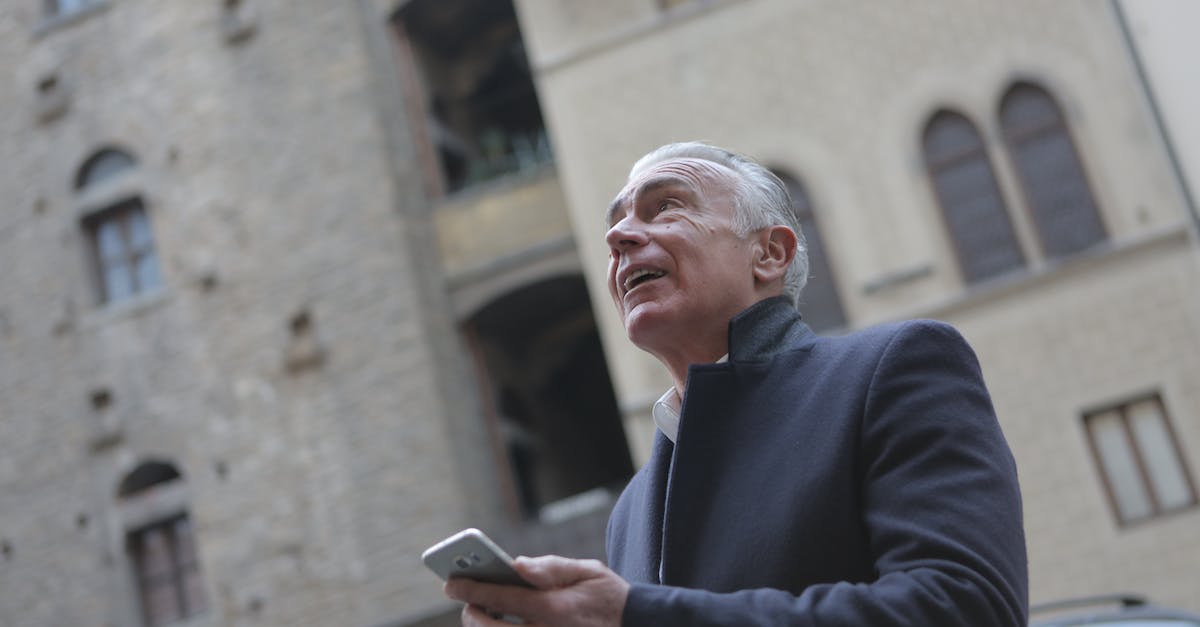 How can I check the age of a city? - From below of mature gentleman in classy wear standing near building in city and checking message on cellphone while looking up How can I check the age of a city? - From below of mature gentleman in classy wear standing near building in city and checking message on cellphone while looking up