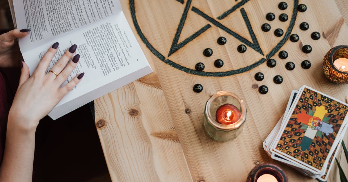 How can I learn the Backstab enchantment in Skyrim through the console? - From above of crop unrecognizable fortune teller reading textbook at table with tarot cards and candles during divination process