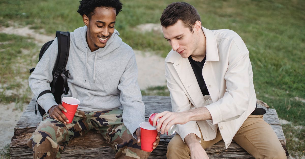 How can I level gathering professions quickly as a high-level character? - High angle of male pouring carbonated drink from tin can to smiling black friend sitting with red cup