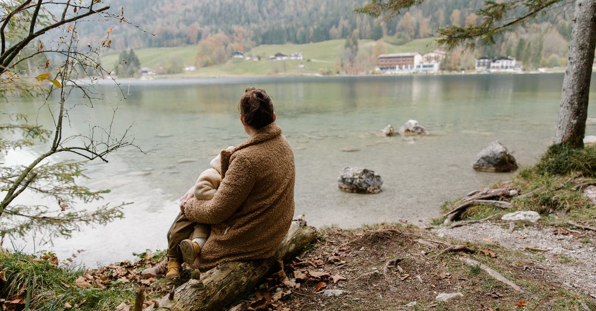 How can I log back in to a Pokemon go account [duplicate] - Back view of unrecognizable mother in casual warm outerwear sitting with baby on hands on log near lake and admiring calm scenery in overcast weather