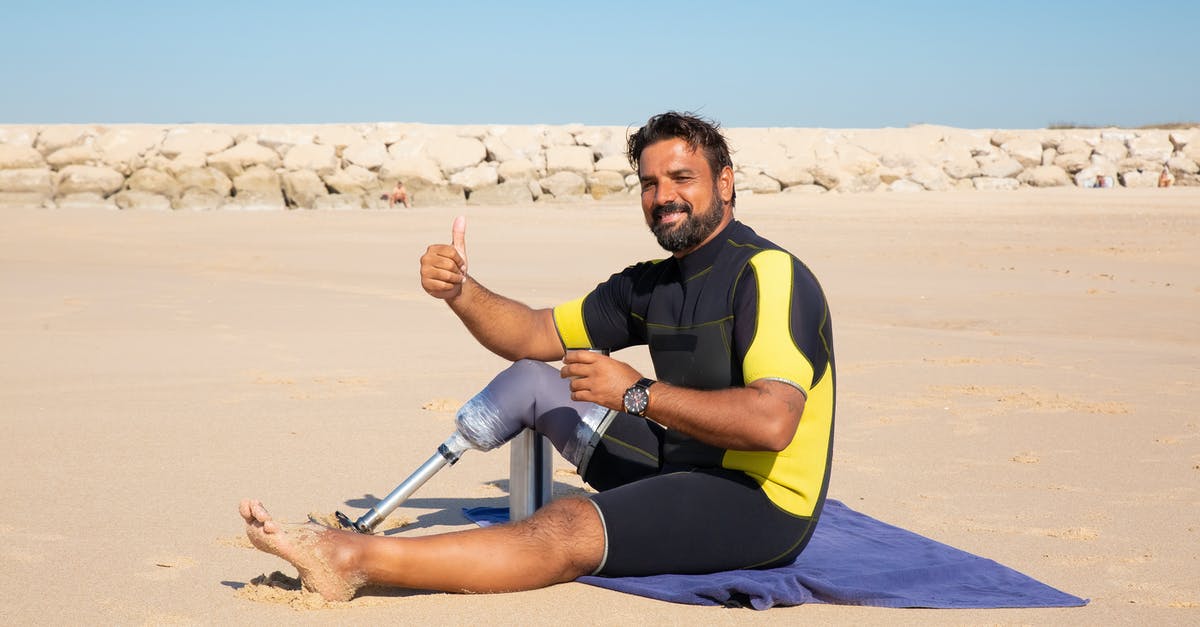 How can I make Strong like me without compromising myself? - Side view full length handsome ethnic man with leg prosthesis resting on sandy seashore and showing thumb up gesture while looking at camera with smile
