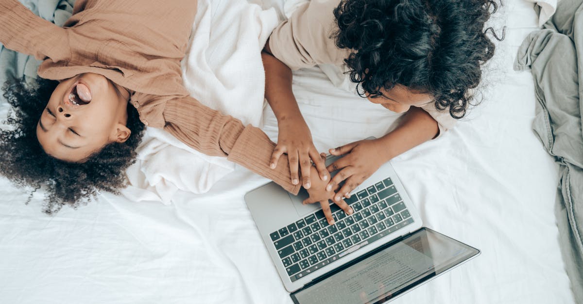 How can I play online with a friend? - Black little child fooling around brother using laptop on bed How can I play online with a friend? - Black little child fooling around brother using laptop on bed