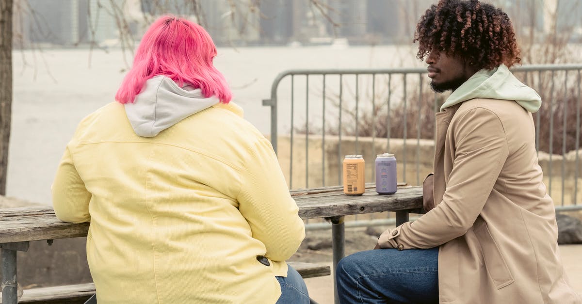 How can I queue spending points? - Stylish African American man and faceless woman with pink hair sitting at wooden table with cans of drinks while spending time on waterfront