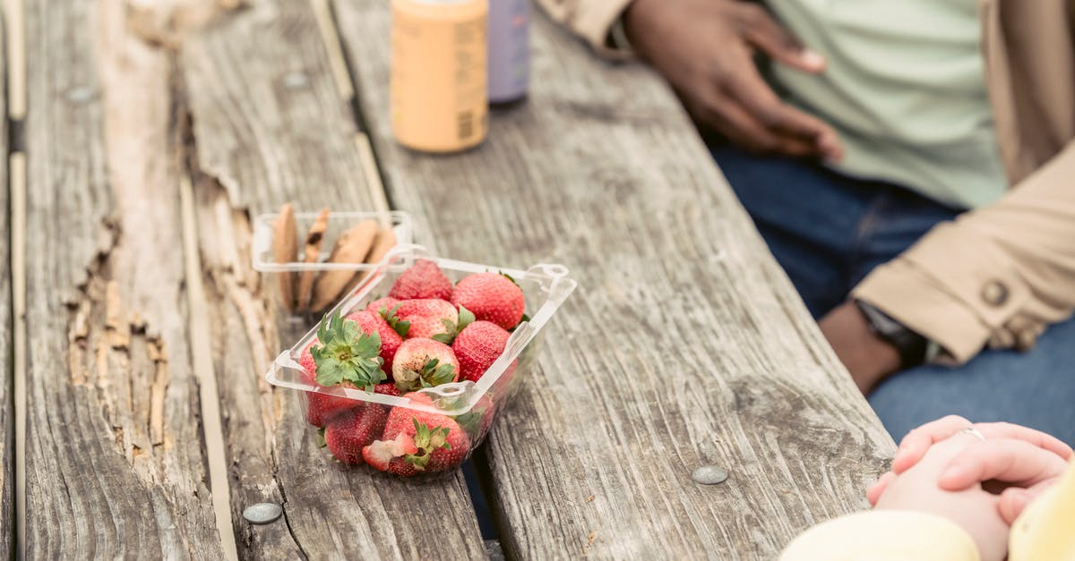 How can I queue spending points? - Crop anonymous couple sitting at shabby wooden table with strawberries and cookies near cans of soda while spending time in park