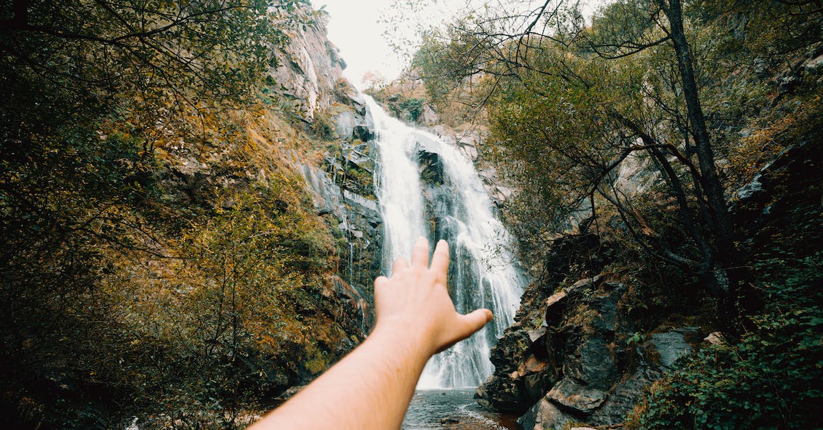 How can I reach the massive tree in the south, near Bald Mountain - Crop person with outstretched hand reaching to cascade of powerful waterfall flowing among rocks covered with moss in summer day in nature How can I reach the massive tree in the south, near Bald Mountain - Crop person with outstretched hand reaching to cascade of powerful waterfall flowing among rocks covered with moss in summer day in nature
