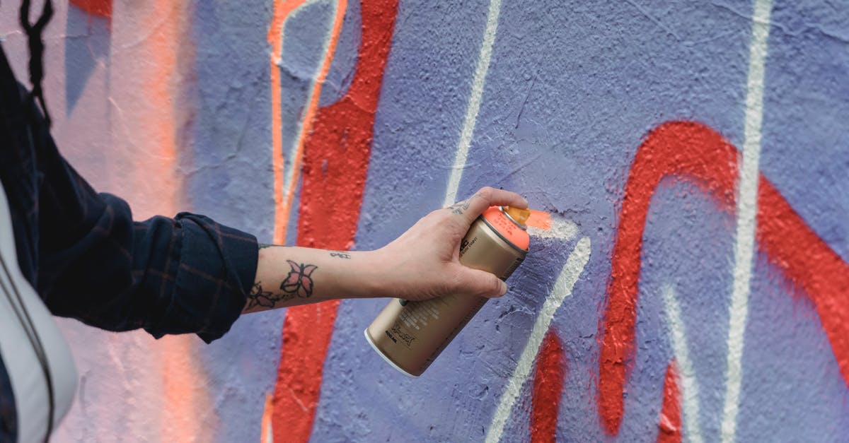 How can I rebuild a razed city? - Crop unrecognizable painter with tattoos in black wear spraying orange paint on colorful purple wall with graffiti on street of city How can I rebuild a razed city? - Crop unrecognizable painter with tattoos in black wear spraying orange paint on colorful purple wall with graffiti on street of city